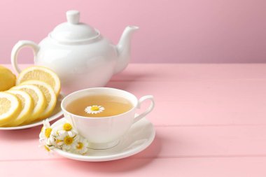 Fincanda nefis papatya çayı, taze çiçekler ve pembe ahşap masada limon, yakın plan. Metin için boşluk