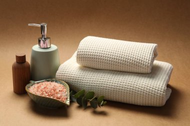 Temiz waffle havluları, deniz tuzu, kozmetik ürünleri ve kahverengi arka planda okaliptüs dalı.