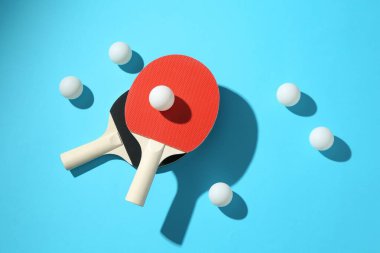 Masa tenisi raketleri ve topları açık mavi arka planda, düz yatıyordu.