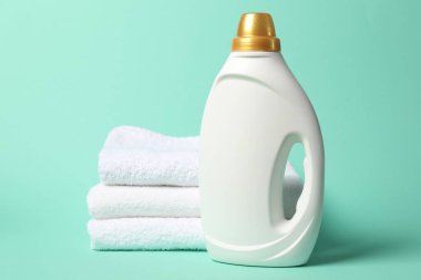 Bir şişe yumuşatıcı ve turkuaz arka planda havlular.