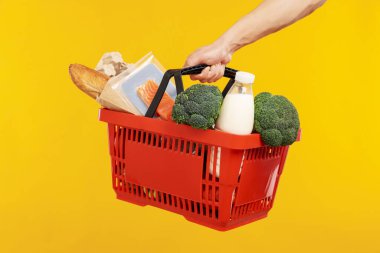 Sarı arka planda farklı ürünleri olan alışveriş sepeti tutan adam, yakın plan.