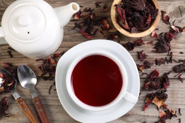 Lezzetli amber çayı fincanda, çaydanlıkta, kuru roselle sepals ve kaşıklar ahşap masada, düz yerde.