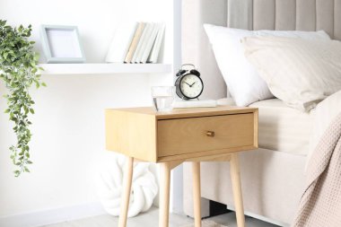 Alarmlı komodinli komodin, bir bardak su ve yatağın yanında kitap.