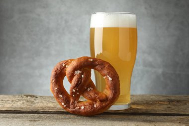 Lezzetli kraker ve bir bardak bira ahşap masada, gri arka planda, yakın planda.