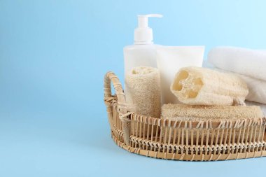 Açık mavi arka planda farklı lif süngerleri, kozmetik ürünleri ve havlular sepette, yakın plan. Metin için boşluk