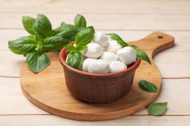 Lezzetli mozzarella peynir topları kasede ve fesleğen açık ahşap masada, yakın plan.