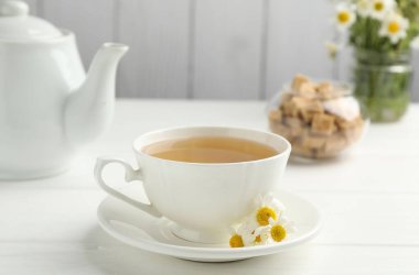 Fincanda nefis papatya çayı, taze çiçekler ve beyaz ahşap masada kahverengi şeker, yakın plan.