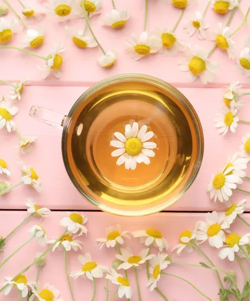 Cam fincanda nefis papatya çayı ve pembe ahşap masada taze çiçekler.