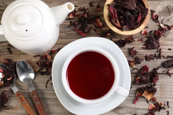 Lezzetli amber çayı fincanda, çaydanlıkta, kuru roselle sepals ve kaşıklar ahşap masada, düz yerde.