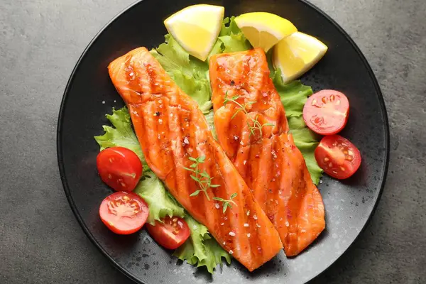 Lezzetli ızgara somon, marul, domates ve limonla servis edilir.