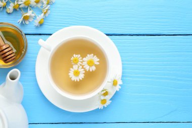 Fincanda nefis papatya çayı, taze çiçekler ve açık mavi ahşap masada bal, düz yatak. Metin için boşluk