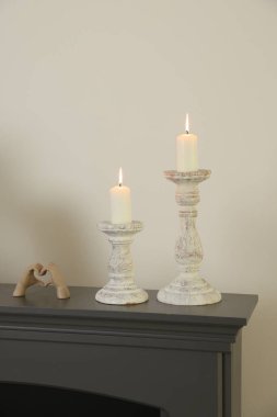 Beyaz duvarın yanındaki şöminede yanan mumlar ve diğer dekorlarla süslü şamdanlar.