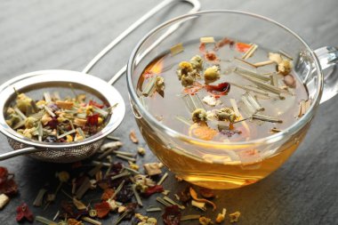 Lezzetli bitkisel çay ve kuru yapraklar siyah masada, yakın plan.