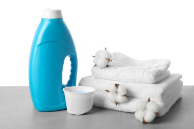 Beyaz arka planda bir şişe yumuşatıcı, pamuk çiçekleri ve havlular.