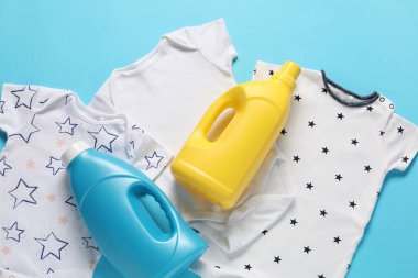 Yumuşatıcı şişeler ve açık mavi arka planda bebek kıyafetleri.
