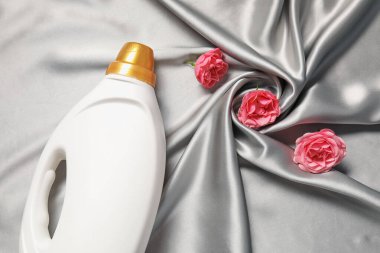 Bir şişe yumuşatıcı ve gri kumaş üzerinde çiçekler, düz yatıyordu.