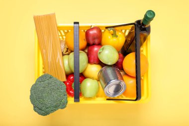 Sarı arka planda ürünlerle dolu plastik alışveriş sepeti.