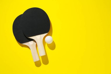Masa tenisi raketleri ve top sarı arka planda, üst manzara. Metin için boşluk