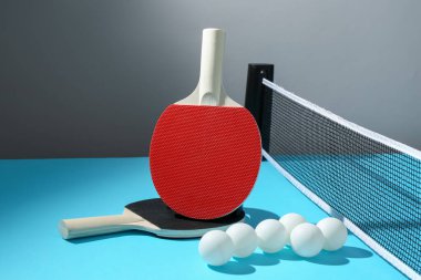 Masa tenisi raketleri, toplar ve ağ açık mavi masada.