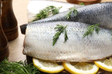 Ahşap masada dereotu ve limon dilimli lezzetli ringa filetoları, yakın plan.