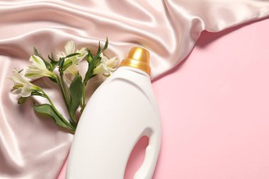 Bir şişe yumuşatıcı, çiçekler ve pembe arka planda bej kumaş, düz yatak. Metin için boşluk