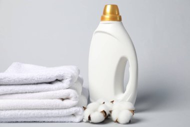 Açık gri arkaplanda bir şişe yumuşatıcı, havlu ve pamuk çiçeği.