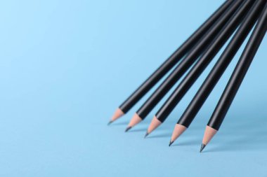 Açık mavi arka planda birçok keskin grafit kalem, yakın plan. Metin için boşluk