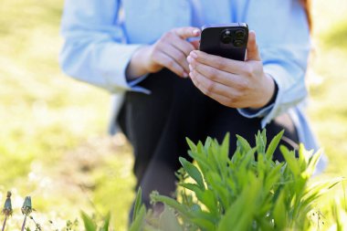 Güneşli bir günde akıllı telefondan bitki tanıma uygulaması kullanan bir kadın.