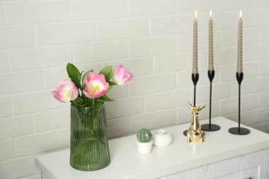 Yanan mumları olan zarif şamdanlar vazoda laleler ve beyaz tuğla duvarın yanındaki şifoniyerde diğer dekorlar.