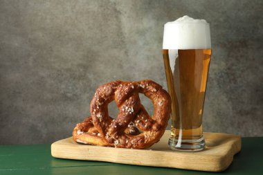 Lezzetli krakerler ve yeşil ahşap masada bir bardak bira. Gri desenli arka plan, yakın plan.