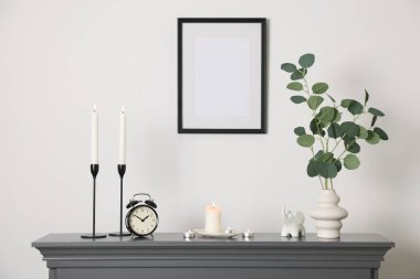 Beyaz duvarın yanındaki şöminede yanan mumlar, diğer dekor ve çalar saat ile şık şamdanlar.