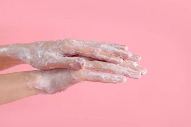 Açık pembe arka planda ellerini sabunla yıkayan kadın, yakın plan.