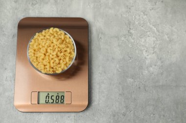 Modern elektronik mutfak terazisi ve gri masa üzerinde bir kase çiğ makarna. Metin için boşluk