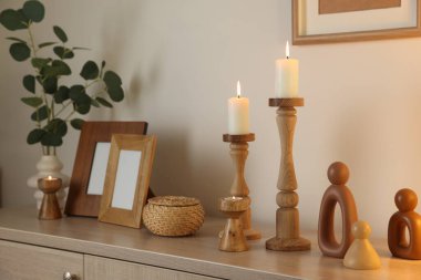 Havalı şamdanlar, yanan mumlar ve kapalı alandaki bej duvarın yanındaki dolaptaki diğer dekorlar.