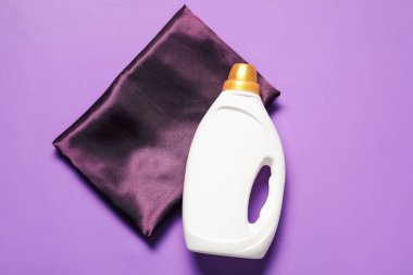 Bir şişe yumuşatıcı ve mor arka planda renk bezi, üst görünüm