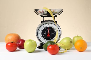 Ürünlerle birlikte mekanik mutfak terazisi ve bej arka planda beyaz ahşap masadaki şerit. Diyet