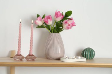 Mumları yanan zarif tutucular, vazoda laleler ve beyaz duvarın yanındaki ahşap masa üzerindeki diğer dekorlar.