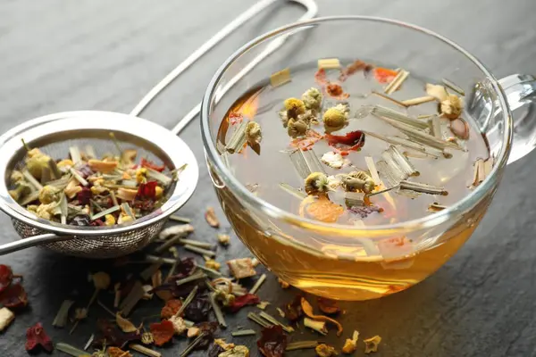 Lezzetli bitkisel çay ve kuru yapraklar siyah masada, yakın plan.