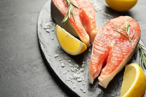 Deniz ürünleri. Siyah desenli masada somon biftekleri, baharatlar ve limon dilimleri, yakın plan.