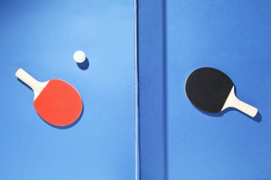 Masa tenisi raketleri, top ve ağ mavi arka planda, düz yatıyordu.