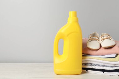 Bir şişe yumuşatıcı, bebek kıyafetleri ve gri arka planda açık ahşap masada duran ayakkabılar. Metin için boşluk