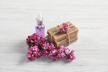 Bir yığın sabun, temel yağ ve leylak çiçekleri beyaz ahşap masada, yakın plan.