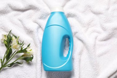 Bir şişe yumuşatıcı ve terli havluda çiçekler, düz uzanmış.