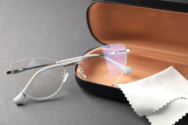 Gri arka planda şık gözlüklü ve temizlik bezli çanta, yakın plan.