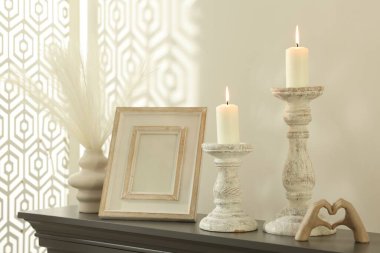 Beyaz duvarın yanındaki şöminede yanan mumlar ve diğer dekorlarla süslü şamdanlar.