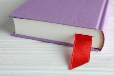 Beyaz ahşap masa üzerinde kırmızı kurdele yer imi olan kitap, yakın plan.