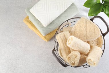 Sepette farklı lif süngeri ve açık gri masa üzerinde düz havlu. Metin için boşluk