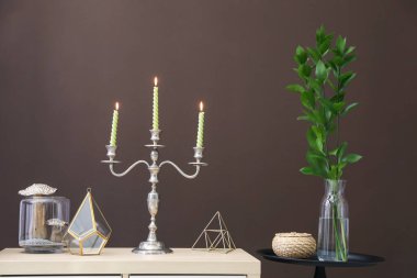 Kahverengi duvarın yanındaki dolapta yanan mumlar ve dekorlar olan zarif bir şamdan.