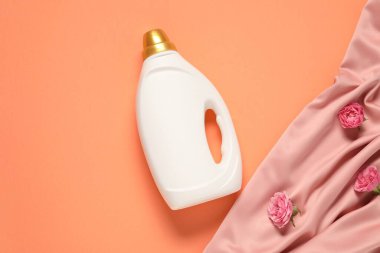 Bir şişe yumuşatıcı, çiçekler ve mercan zemin üzerinde pembe kumaş, düz uzanmış.