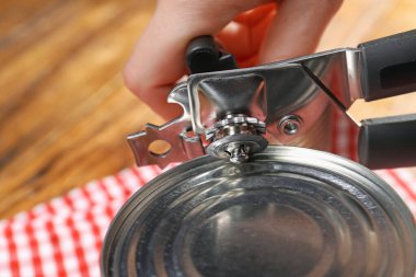 Kadın konserve açacağıyla konserve açıyor. Ahşap masada, yakın plan.